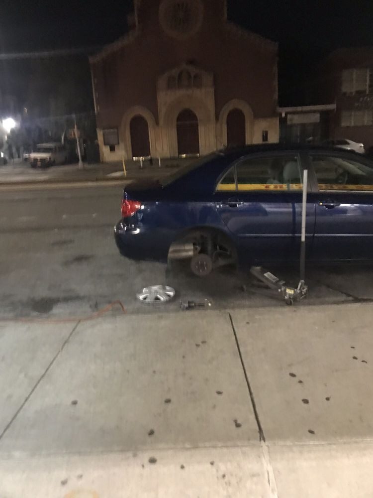 A car up on a jack outside the shop with a wheel off
